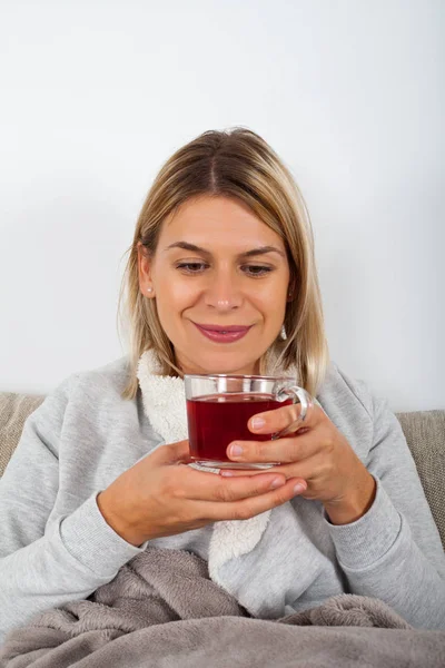 Atraktivní Blondýnka Pití Horkého Čaje Zatímco Sedí Gauči Zabalený Šedé — Stock fotografie