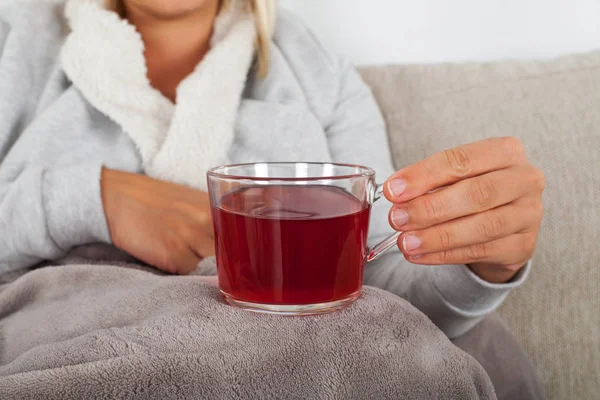 ソファに座って暖かい毛布に包まれながら熱いお茶のカップを保持している病気の女性の写真を閉じる — ストック写真
