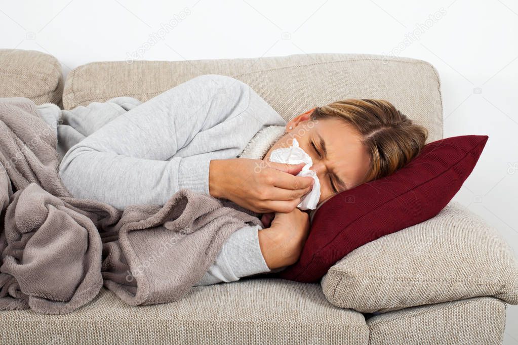Sick woman lying on the sofa blowing her nose - sinus infection