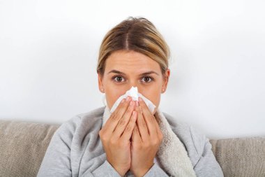 Kanepede oturan ve onun burun akıntısı üfleme hasta genç bir kız resim