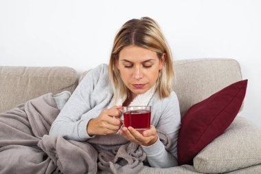 Kanepede rahatlatıcı ve gri bir battaniyeye sarılmış sıcak çay içme güzel kadın