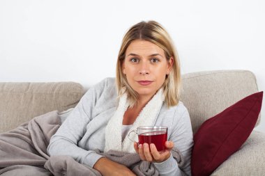 Kanepede rahatlatıcı ve gri bir battaniyeye sarılmış sıcak çay içme güzel kadın