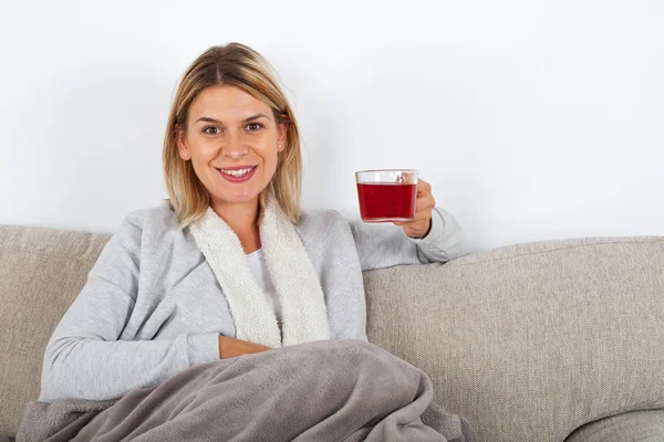 ソファでリラックスと熱いお茶で 灰色の毛布に包まれた美しい女性 — ストック写真
