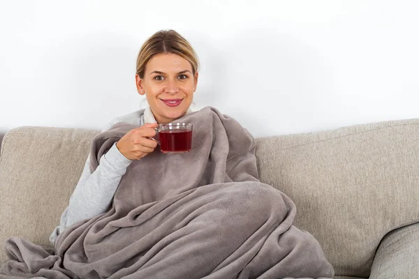 熱いお茶を飲むと ナプキンを保持しながらソファで休んで病気の若い女性 — ストック写真