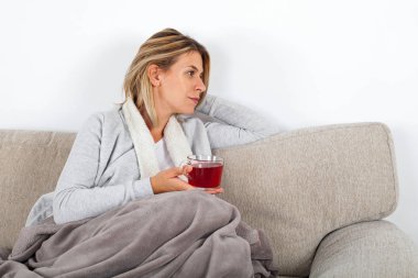 Kanepede rahatlatıcı ve gri bir battaniyeye sarılmış sıcak çay içme güzel kadın