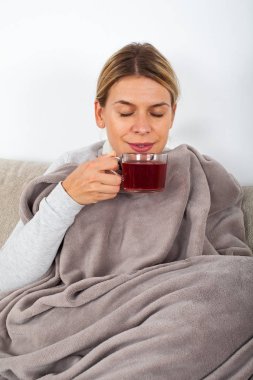 Hasta genç kadın kanepede sıcak çay içme ve peçeteler tutarak dinlenme