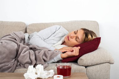 Genç kadın mevsimsel grip olan thesofa üzerinde dinlenme, sıcak çay içme ve ilaç