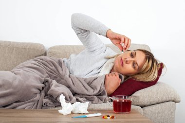 Genç kadın mevsimsel grip olan thesofa üzerinde dinlenme, sıcak çay içme ve ilaç