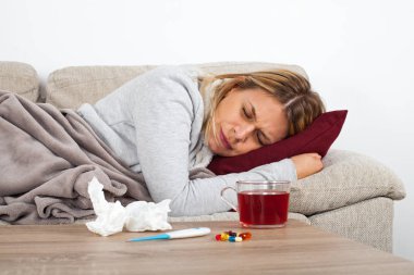 Genç kadın mevsimsel grip olan thesofa üzerinde dinlenme, sıcak çay içme ve ilaç