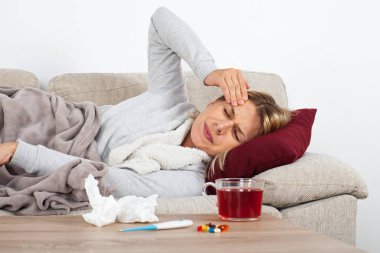 Genç kadın mevsimsel grip olan thesofa üzerinde dinlenme, sıcak çay içme ve ilaç
