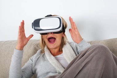 Kanepede oturan ve bir sanal gerçeklik kulaklık zevk neşeli genç kadın