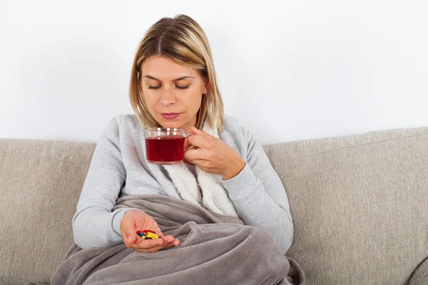 季節性インフルエンザを持っている若い女性の Thesofa で休んで 熱いお茶を飲むと薬の服用 — ストック写真