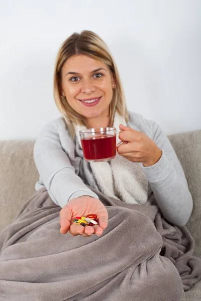 季節性インフルエンザを持っている若い女性の Thesofa で休んで 熱いお茶を飲むと薬の服用 — ストック写真