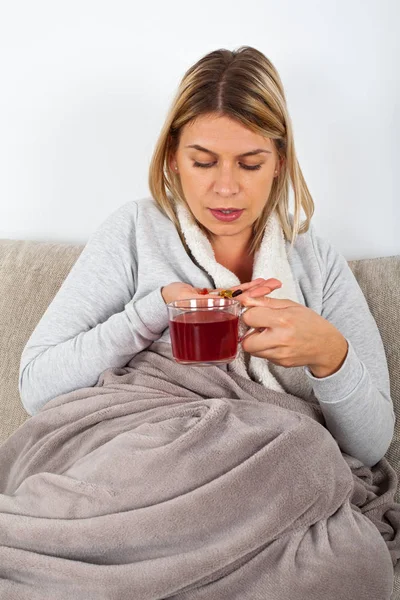 有季节性流感的年轻妇女休息在沙发 喝热茶和服药 — 图库照片