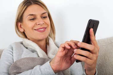 Güzel sarışın kadın kanepede rahatlatıcı ve onun akıllı telefon kısa mesaj yazma