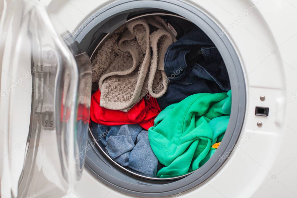 Modern automatic washing machine loaded with colorful clothes