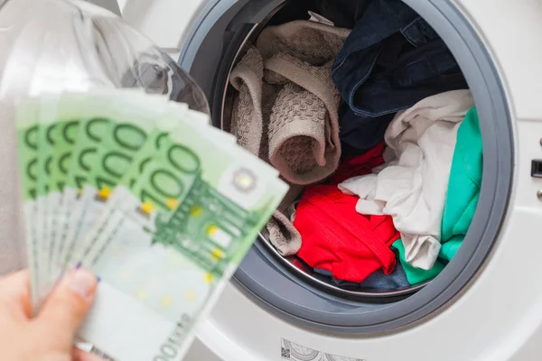 Human hand holding money in front of washing machine loaded with laundry - Euro currency