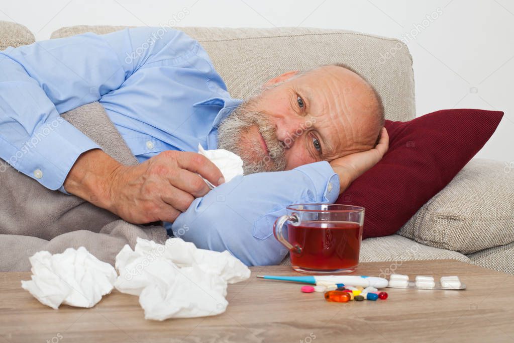 Sick senior male patient lying on the couch at home