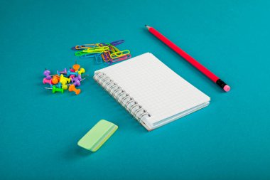 Beyaz defter, kalem ve renkli kağıt kırpmak üstünde mavi arka plan - okul kavramı malzemeleri