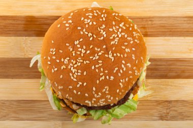 Sığır eti, kaşar ve susam çörek içinde marul ile lezzetli duble çizburger resmini kapatın. Üstten görünüm. Ahşap arka plan