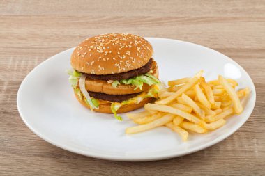 Taze lezzetli duble çizburger sığır, kaşar ve marul ve beyaz tabakta, ahşap masa patates kızartması ile
