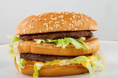 Sığır eti, çedar, susam çörek içinde marul ile lezzetli bir duble çizburger resmini kapatın