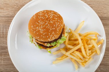 Taze lezzetli duble çizburger sığır, kaşar ve marul ve beyaz tabakta, ahşap masa patates kızartması ile
