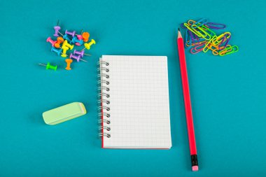 Beyaz defter, kalem ve renkli kağıt kırpmak üstünde mavi arka plan - okul kavramı malzemeleri
