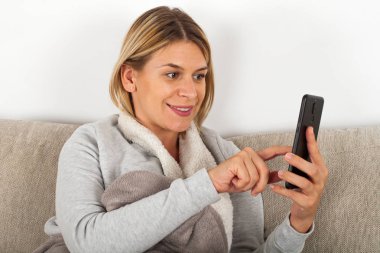 Manifatura telefon arkadaş evde kanepede oturan mevsimsel grip, güzel genç kadın
