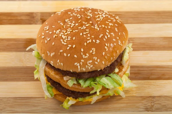 Close up picture of delicious double cheeseburger with beef, cheddar and lettuce in a sesame bun. Top view. Wooden background