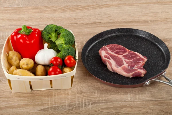 新鲜蔬菜和美味的猪肉牛排在木制背景的不粘煎锅 — 图库照片