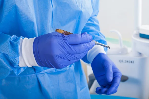 Close up picture of dental surgeon wearing blue gloves and coat, holding a dental drill