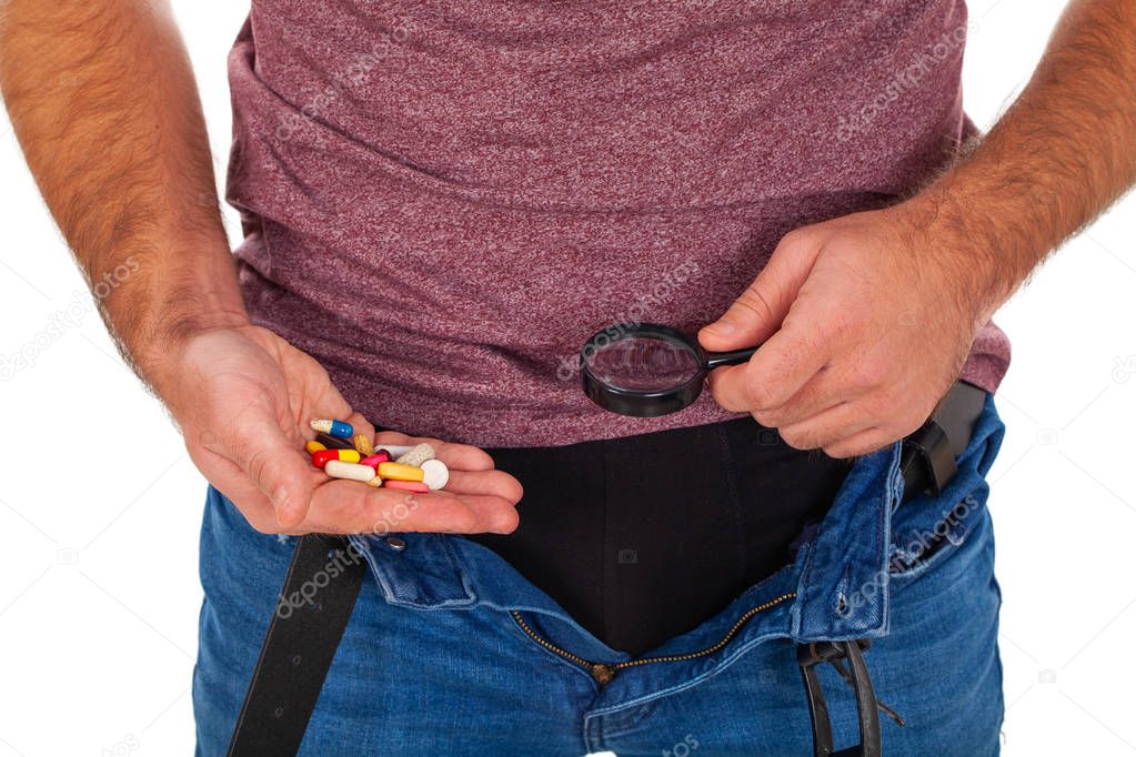 Close up picture of man's crotch with unzipped jeans holding potency pills and enlarged viewer