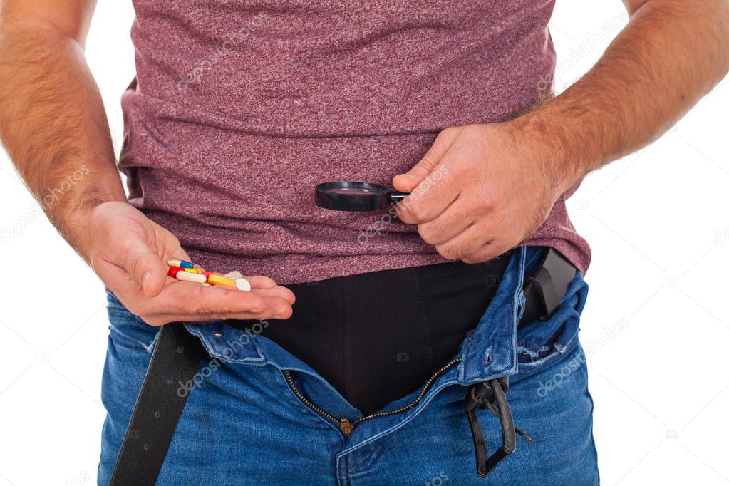 Close up picture of man's crotch with unzipped jeans holding potency pills and enlarged viewer