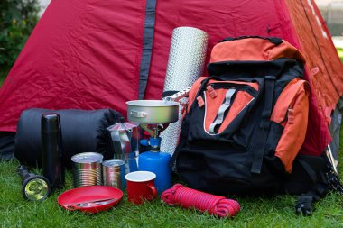 Otların üzerindeki kamp aletlerinin resmi - sırt çantası, çadır, benzin deposu, teneke kutu, pusula, vs. - ormana gitmeye hazır.