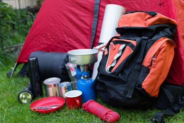 Otların üzerindeki kamp aletlerinin resmi - sırt çantası, çadır, benzin deposu, teneke kutu, pusula, vs. - ormana gitmeye hazır.