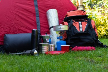 Otların üzerindeki kamp aletlerinin resmi - sırt çantası, çadır, benzin deposu, teneke kutu, pusula, vs. - ormana gitmeye hazır.