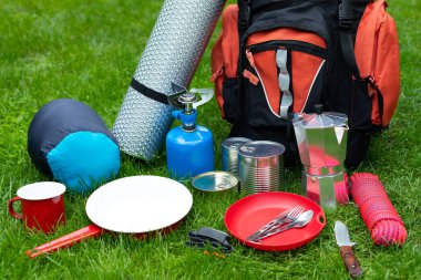 Otların üzerindeki kamp aletlerinin resmi - sırt çantası, çadır, benzin deposu, teneke kutu, pusula, vs. - ormana gitmeye hazır.