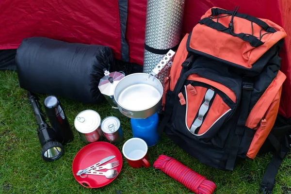 Picture of camping tools on the grass - backpack, tent, gas tank, cans, compass, etc - ready to go in the woods