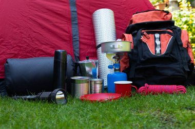 Otların üzerindeki kamp aletlerinin resmi - sırt çantası, çadır, benzin deposu, teneke kutu, pusula, vs. - ormana gitmeye hazır.