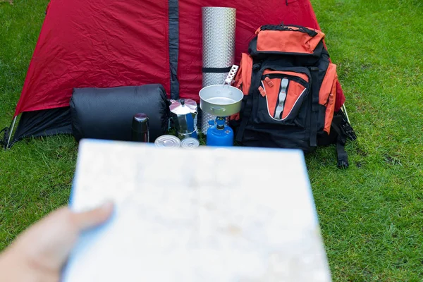 Picture of camping tools on the grass - backpack, tent, gas tank, cans, compass, etc - ready to go in the woods