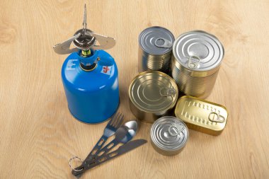 Bir masanın üzerindeki kamp aletlerinin resmi - benzin deposu, teneke kutu, vs. - ormana gitmeye hazır. 