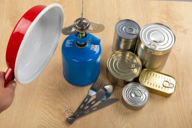 Bir masanın üzerindeki kamp aletlerinin resmi - benzin deposu, teneke kutu, vs. - ormana gitmeye hazır. 