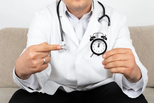 Male doctor holding a black clock in his hands