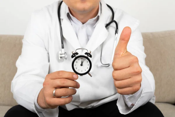 Male doctor holding a black clock in his hands