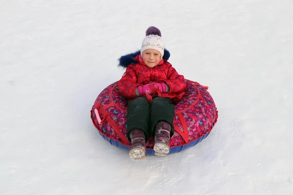 女孩在一个充气雪橇骑从雪坡 — 图库照片