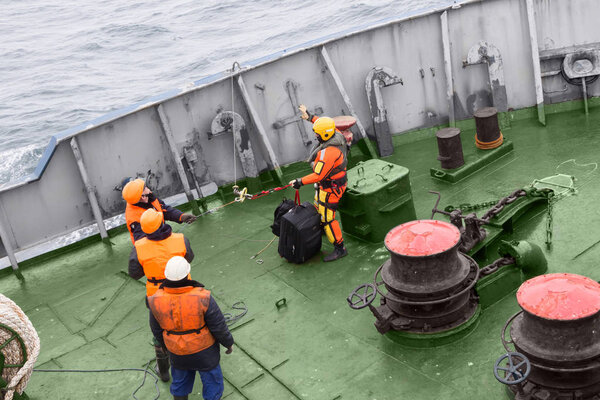 seamen carry out a rescue operation on the deck of a ship,person are preparing to lift the cord from the deck of the ship to the helicopter