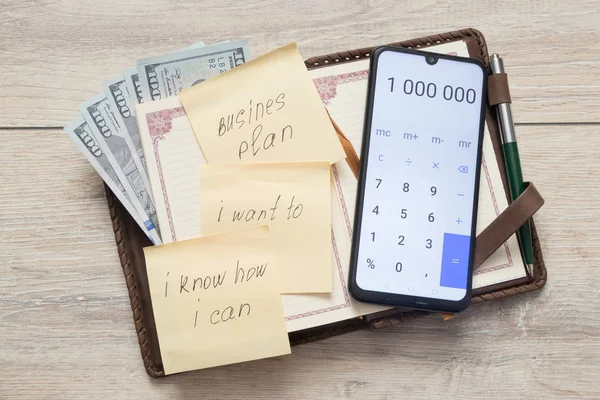 bize dolar ile Organizatör ve açık hesap makinesi numaraları 1 000 000 ve yapışkan notu ile bir yazıt ile işletme planı, ben istiyorum, ben biliyorum ne kadar ben bir masa arka plan üzerinde Can sac