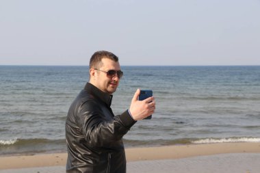 güneş gözlüğü adam ve siyah ceket deniz tarafından bir akıllı telefonda bir mesaj okuma