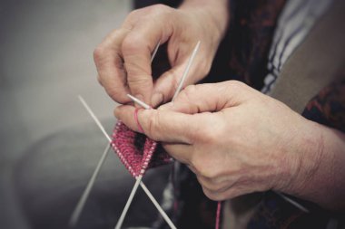 Yaşlı bir kadın elinde yün iplik örgü iğneleri ile kıyafetlerden örgü